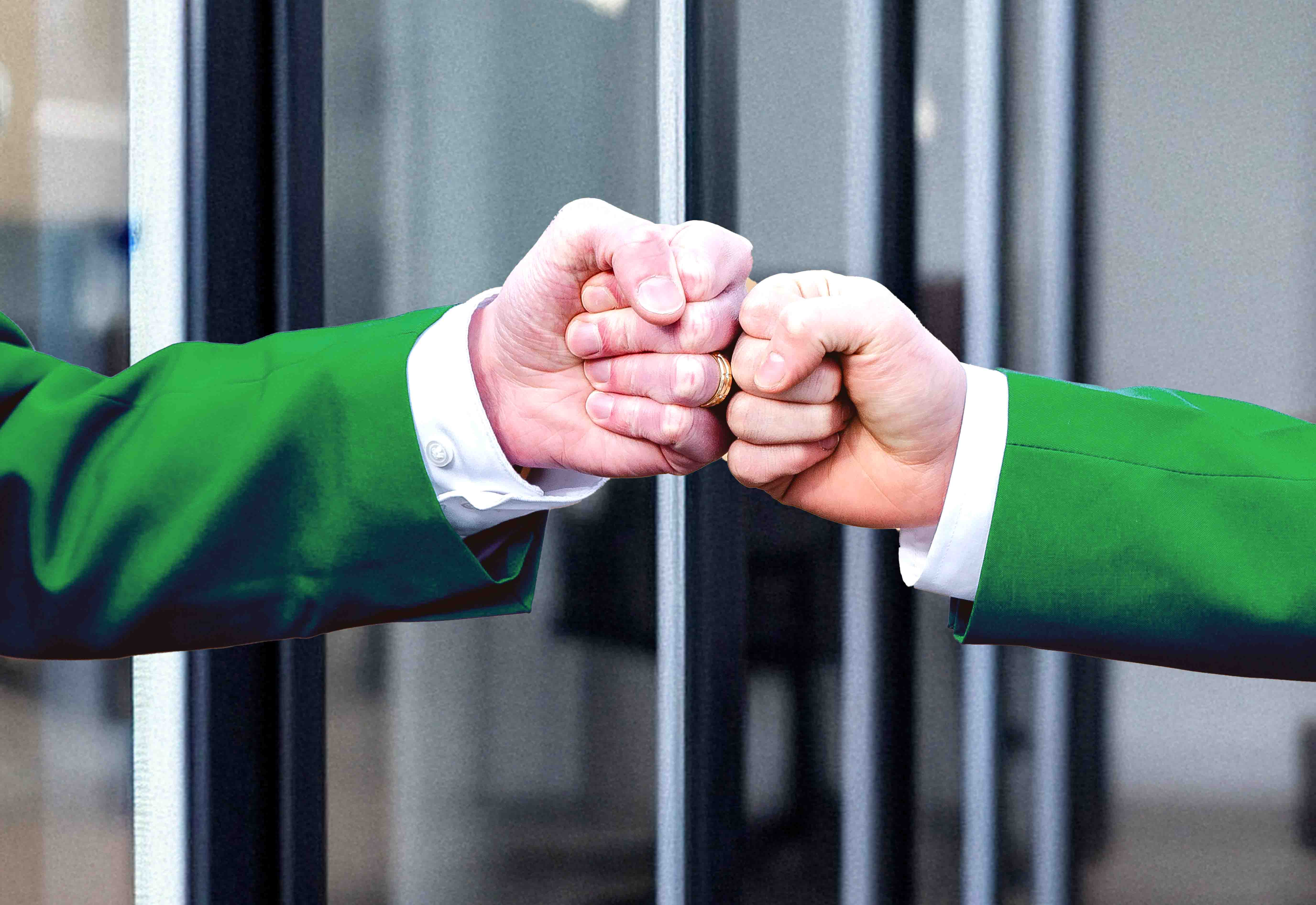 Two fists bumping in an office in green suits.