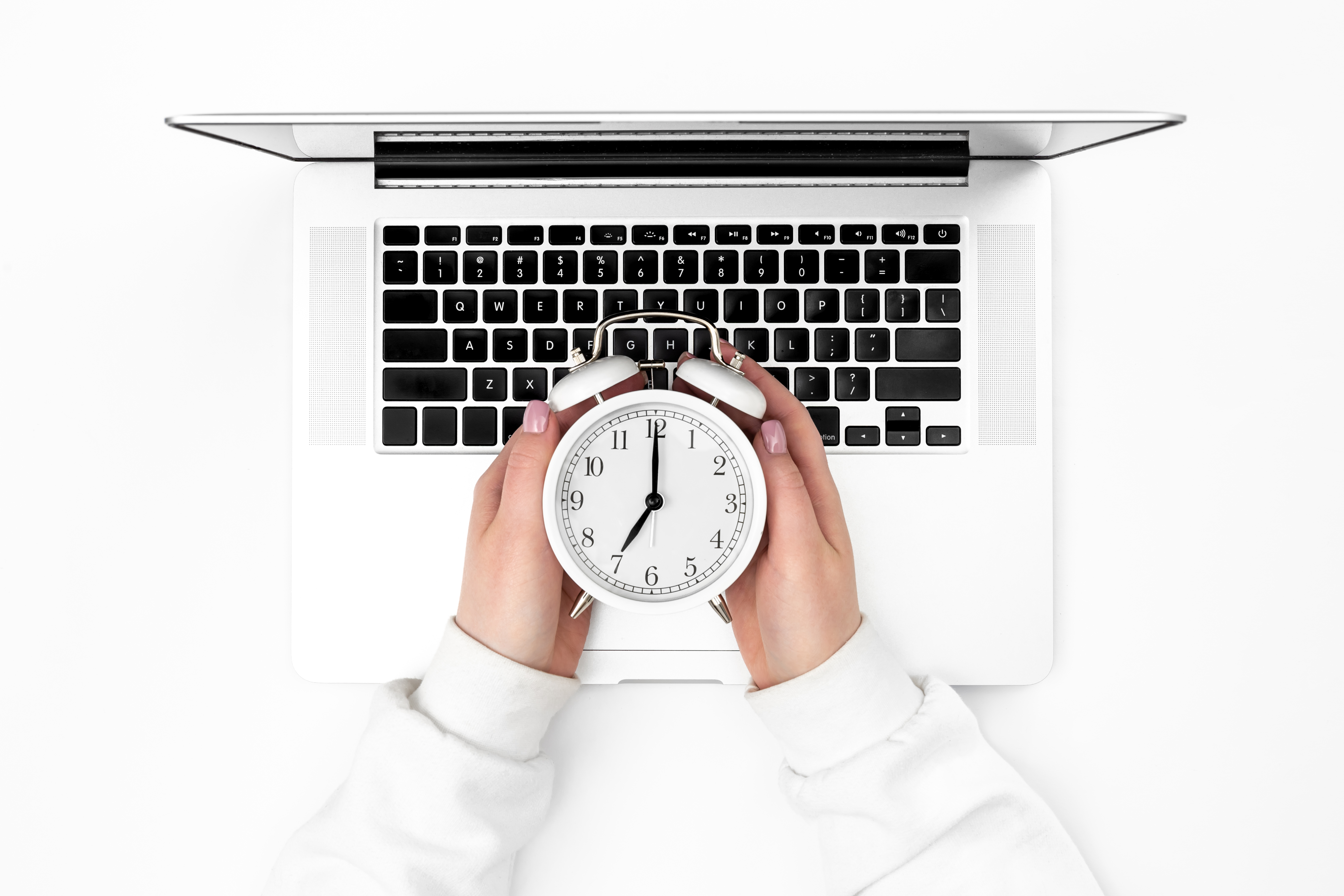 Person holding a clock in front of open laptop.